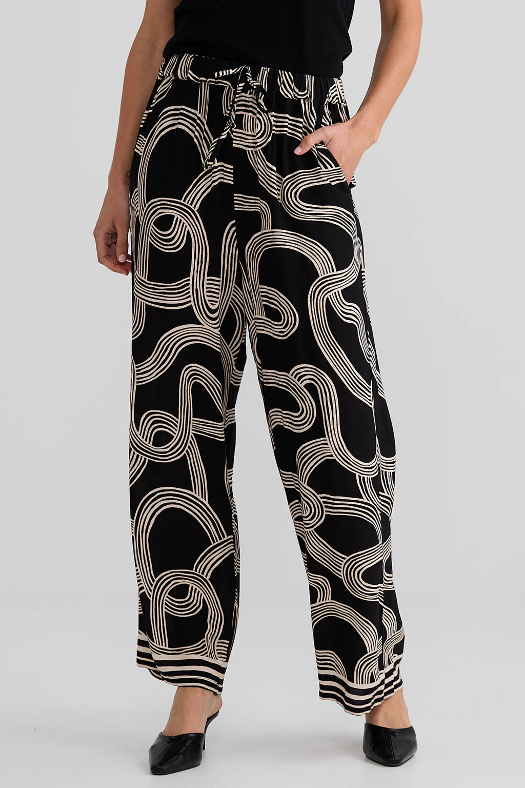 Relaxed straight-leg pants with an elasticated drawstring waistband, cutaway side pockets, lightweight draping fabric, and bold abstract line print.