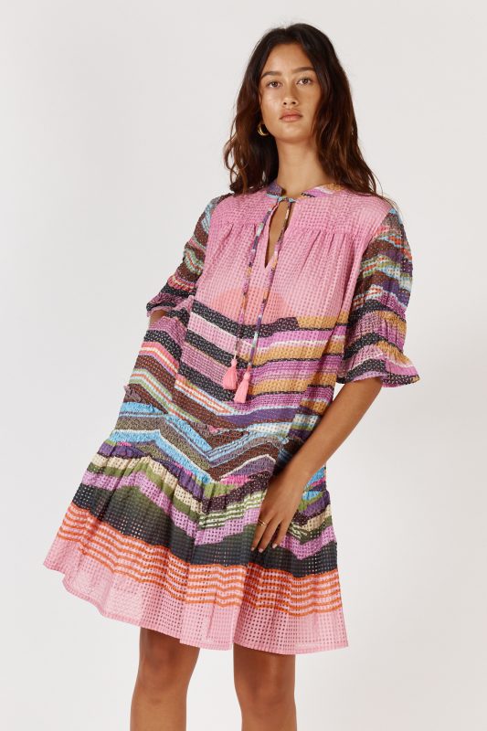 A knee-length dress made from a textured check-weave cotton-nylon blend, featuring a V-neckline with an adjustable tie that can create a rounded neckline. The design includes soft short puff sleeves, a relaxed drop waist, and an easy, feminine silhouette. Lightweight and comfortable, the dress offers a stylish, versatile look suitable for day or night