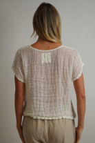 A relaxed, cropped white top made from handloomed stonewashed linen with an open weave fabric, perfect for layering over high-waisted pants or skirts.