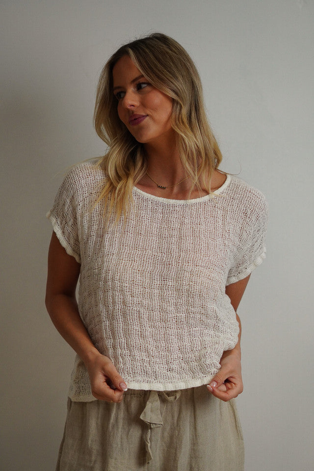 A relaxed, cropped white top made from handloomed stonewashed linen with an open weave fabric, perfect for layering over high-waisted pants or skirts.