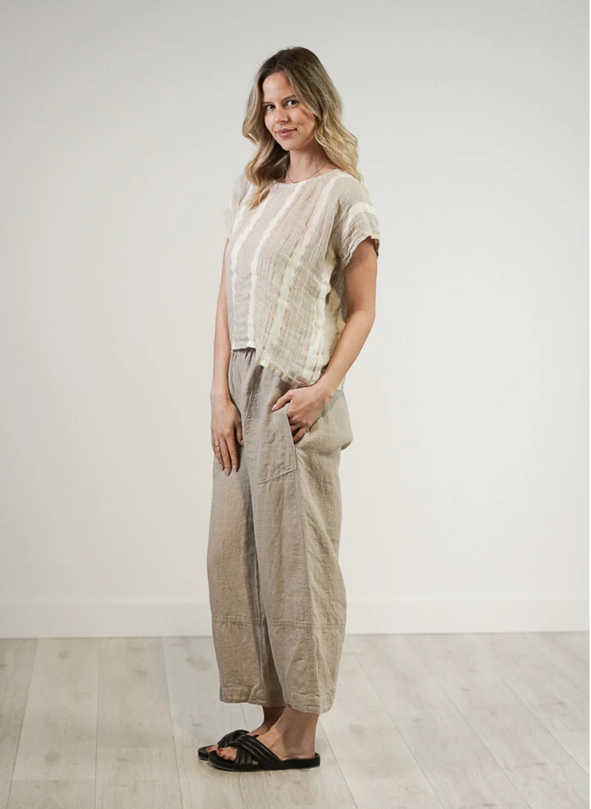 A natural white, box-fit top made from 100% stonewashed mesh linen, featuring short sleeves and a crew neckline. The airy, breathable fabric and relaxed silhouette offer a soft, comfortable feel with subtle gold strand detailing