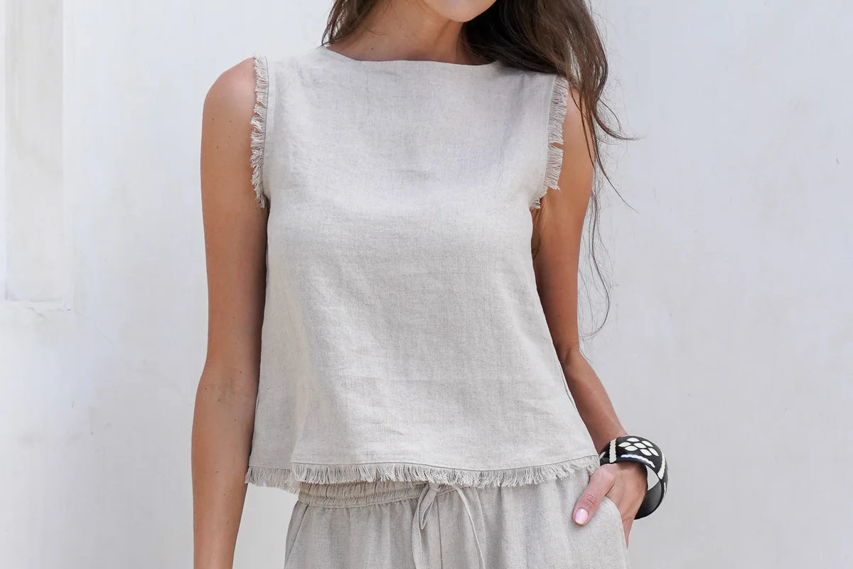 Natural French linen coastal top with a relaxed fit, soft frayed edges, and button opening at the back, styled for easy summer wear.