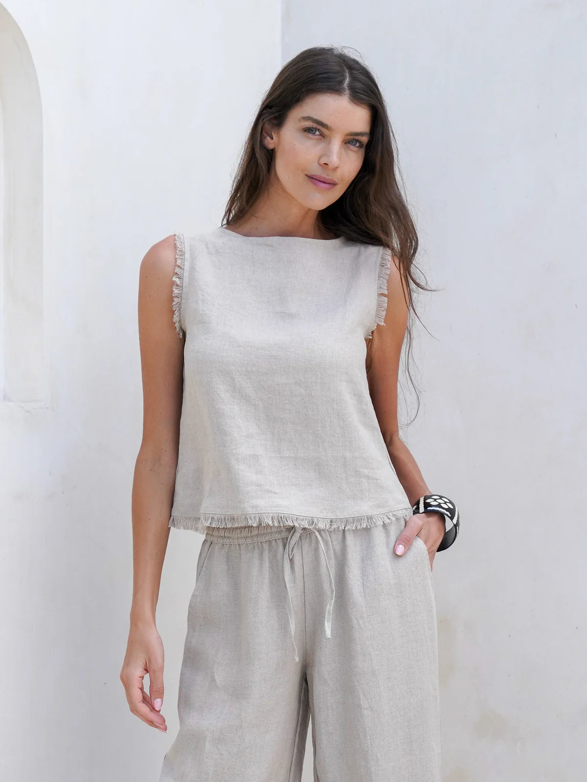 Natural French linen coastal top with a relaxed fit, soft frayed edges, and button opening at the back, styled for easy summer wear.