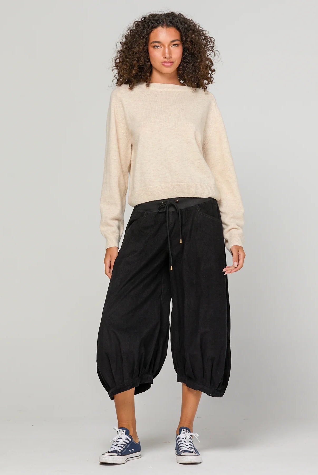 Woman wearing Boom Shankar Cord Guru Pants in soft cotton corduroy with a relaxed balloon-leg fit and 3/4 length style, standing in a coastal boutique setting.