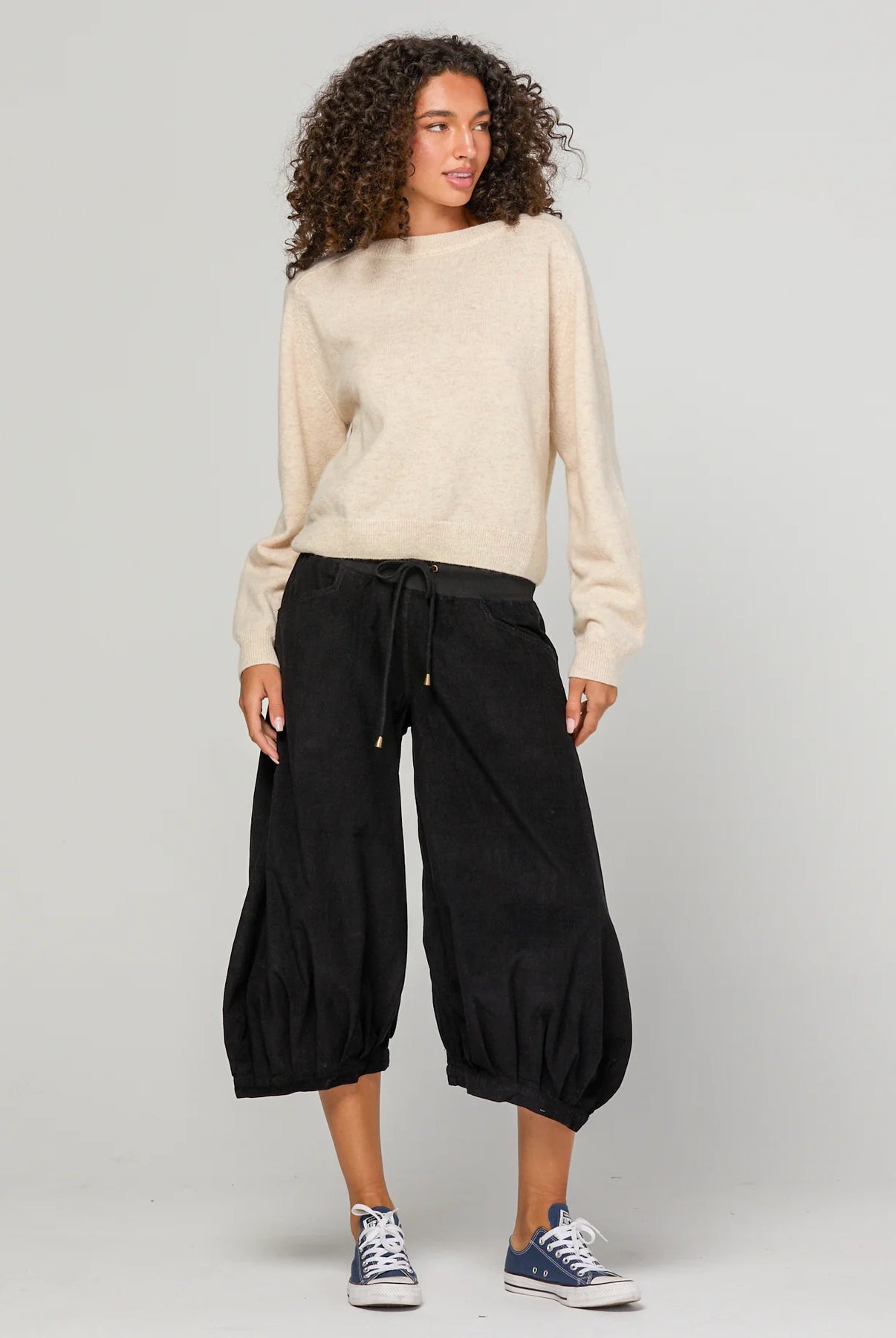 Woman wearing Boom Shankar Cord Guru Pants in soft cotton corduroy with a relaxed balloon-leg fit and 3/4 length style, standing in a coastal boutique setting.