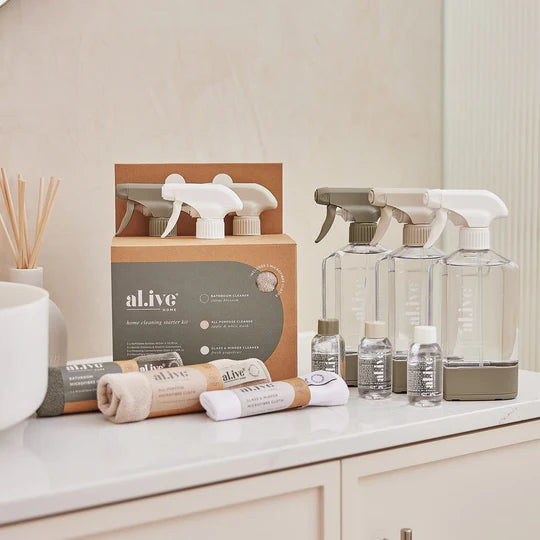 The Al.ive Home Cleaning Starter Kit, featuring three refillable 450ml bottles, each paired with 50ml cleaning concentrates for All Purpose, Bathroom, and Glass & Mirror cleaning. The kit includes three microfibre cloths, three bottle stations with connectors for customizable organization, and a sleek, modern design displayed on a clean countertop. The eco-friendly packaging is made with 30% post-consumer recycled plastic, showcasing a sustainable and effective cleaning solution.