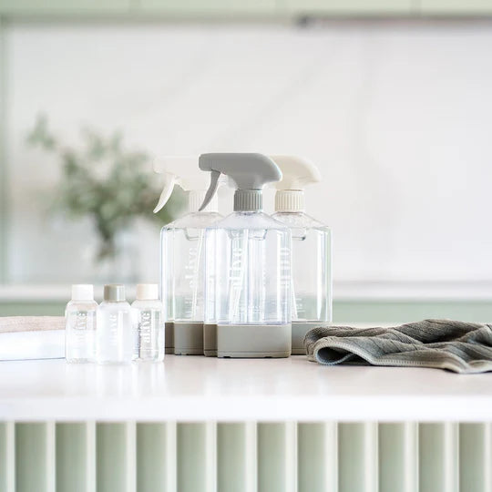 The Al.ive Home Cleaning Starter Kit, featuring three refillable 450ml bottles, each paired with 50ml cleaning concentrates for All Purpose, Bathroom, and Glass & Mirror cleaning. The kit includes three microfibre cloths, three bottle stations with connectors for customizable organization, and a sleek, modern design displayed on a clean countertop. The eco-friendly packaging is made with 30% post-consumer recycled plastic, showcasing a sustainable and effective cleaning solution.