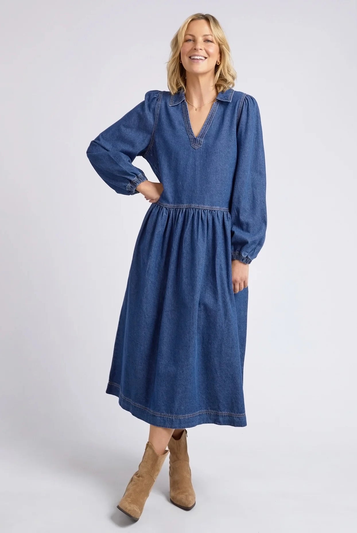 Dark blue wash Josephine Denim Dress by Elm with a V-neck, small collar, gathered waist, puffed long sleeves, and side pockets, crafted from 100% cotton.