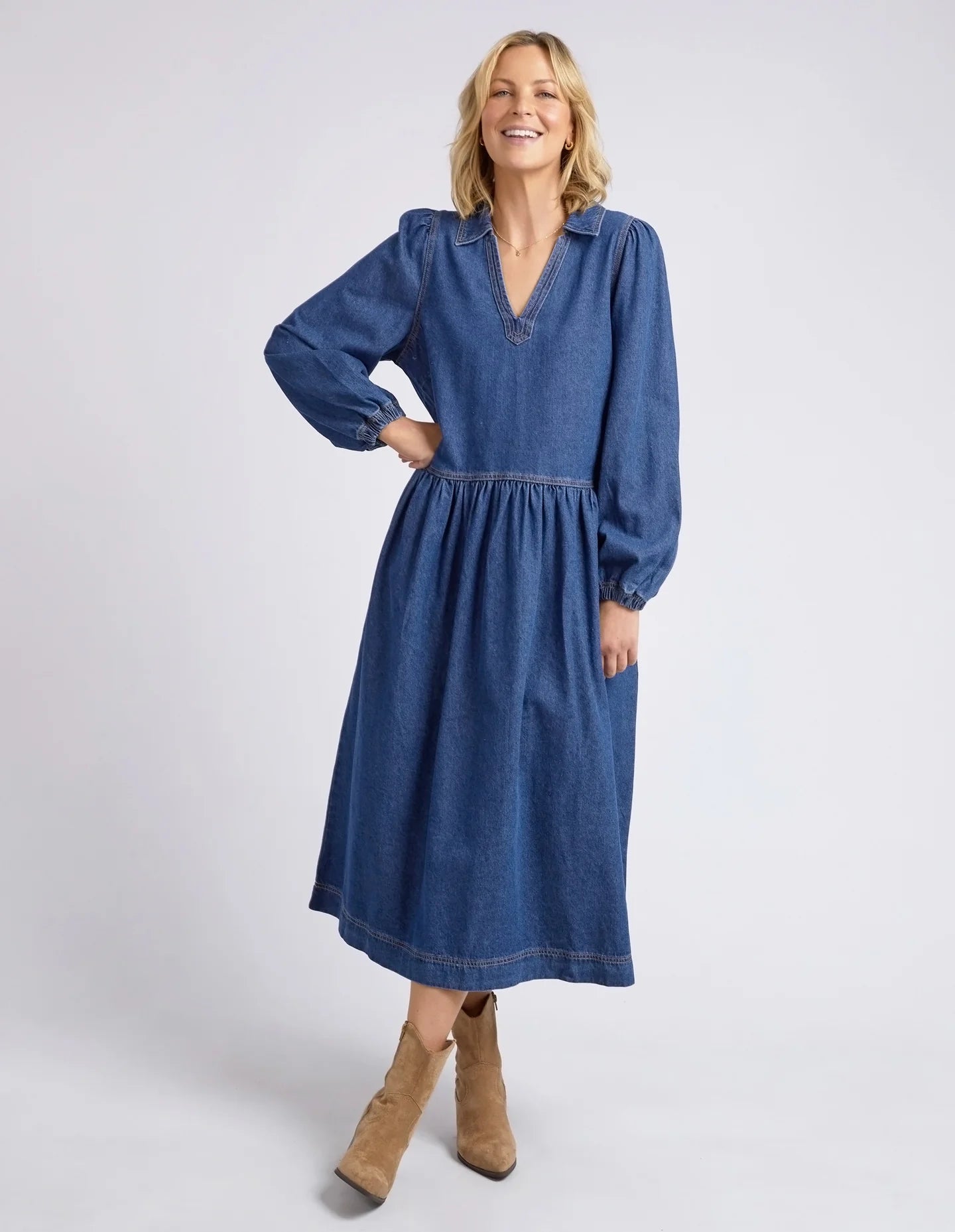 Dark blue wash Josephine Denim Dress by Elm with a V-neck, small collar, gathered waist, puffed long sleeves, and side pockets, crafted from 100% cotton.