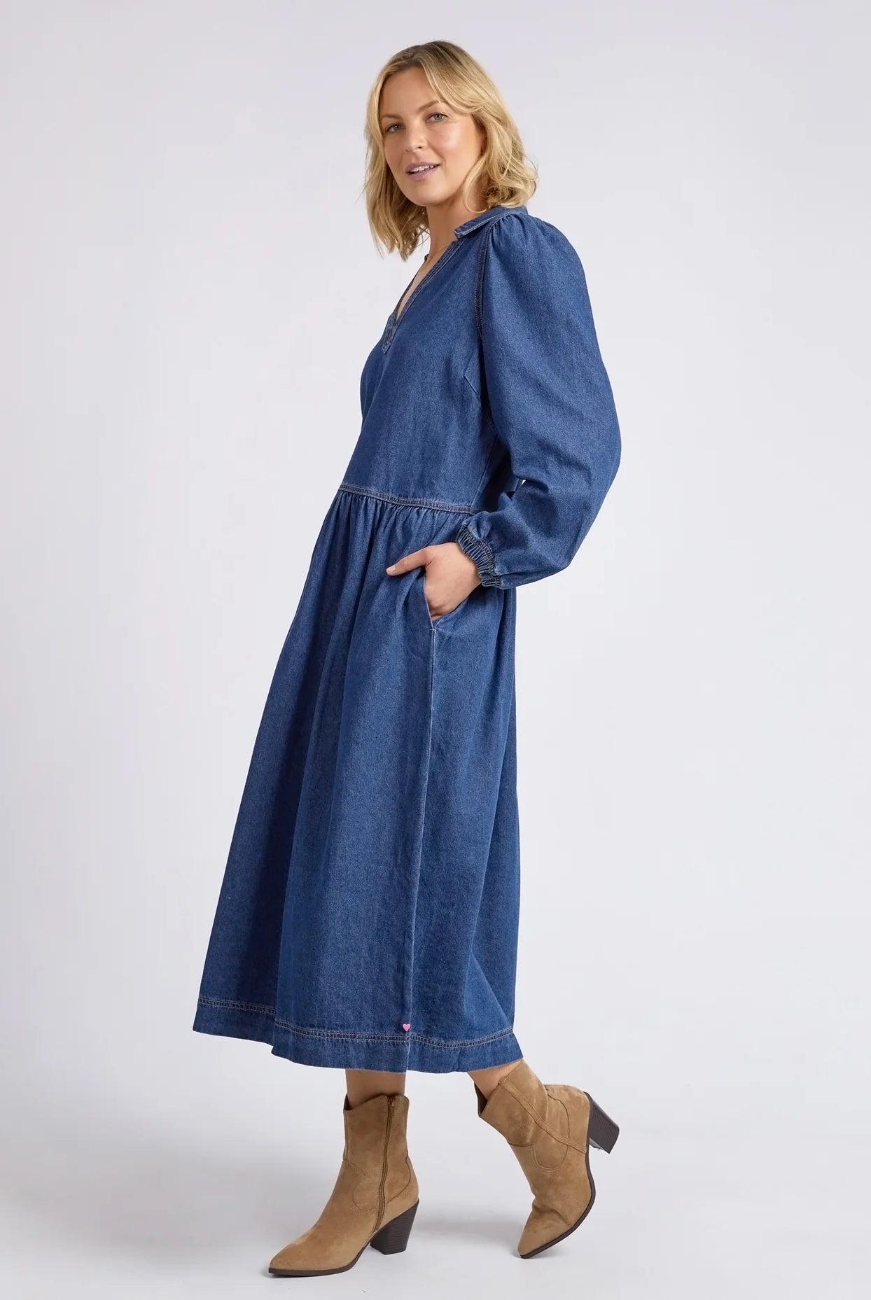 Dark blue wash Josephine Denim Dress by Elm with a V-neck, small collar, gathered waist, puffed long sleeves, and side pockets, crafted from 100% cotton.