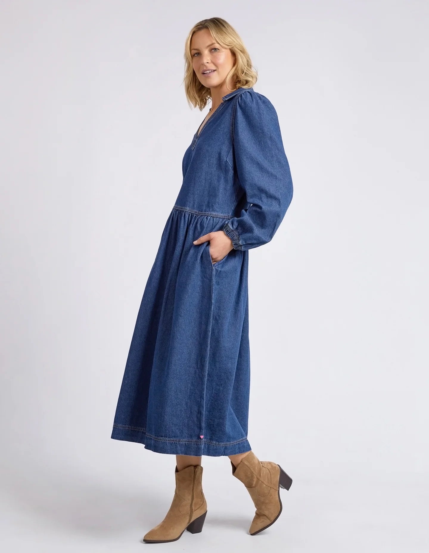 Dark blue wash Josephine Denim Dress by Elm with a V-neck, small collar, gathered waist, puffed long sleeves, and side pockets, crafted from 100% cotton.