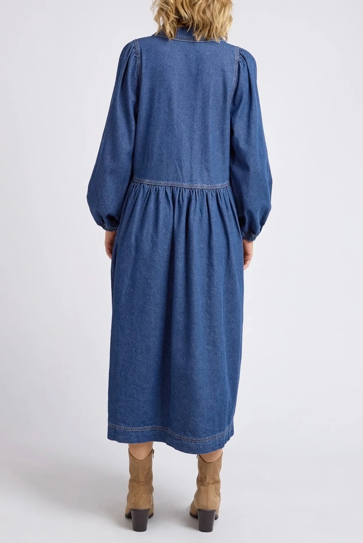 Dark blue wash Josephine Denim Dress by Elm with a V-neck, small collar, gathered waist, puffed long sleeves, and side pockets, crafted from 100% cotton.