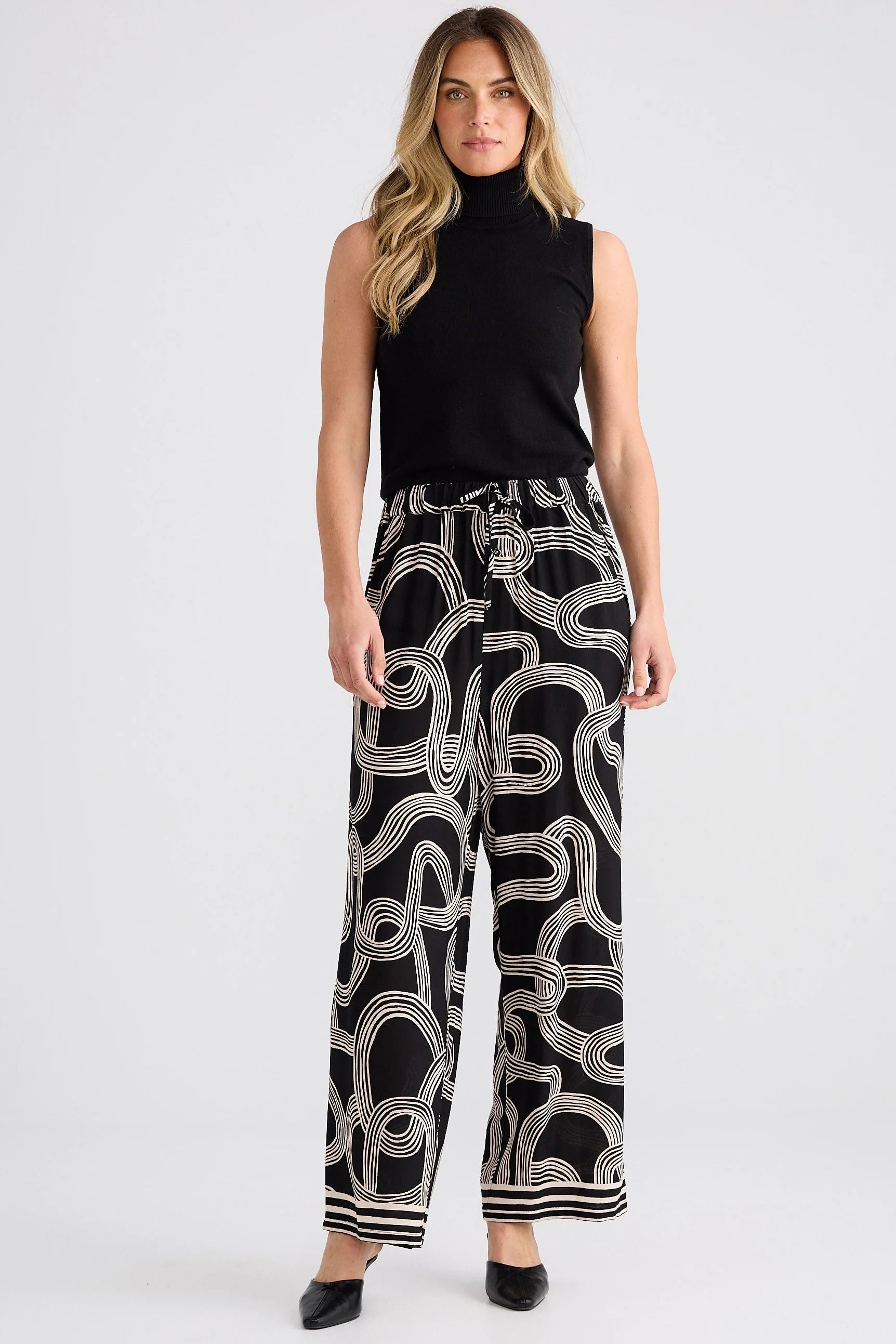 Relaxed straight-leg pants with an elasticated drawstring waistband, cutaway side pockets, lightweight draping fabric, and bold abstract line print.