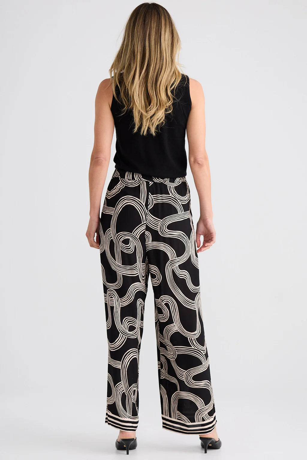Relaxed straight-leg pants with an elasticated drawstring waistband, cutaway side pockets, lightweight draping fabric, and bold abstract line print.
