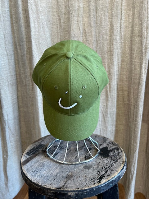 Smiley Cap in Olive with curved brim, adjustable back strap, and embroidered smiley face detail on the front.