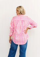 Woman wearing the Tilly Shirt in pastel pink and orange print, featuring a ruffled stand collar, button front, and lightweight cotton fabric, styled for a relaxed beachside look.