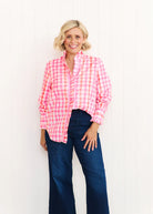 Woman wearing the Tilly Shirt in pastel pink and orange print, featuring a ruffled stand collar, button front, and lightweight cotton fabric, styled for a relaxed beachside look.