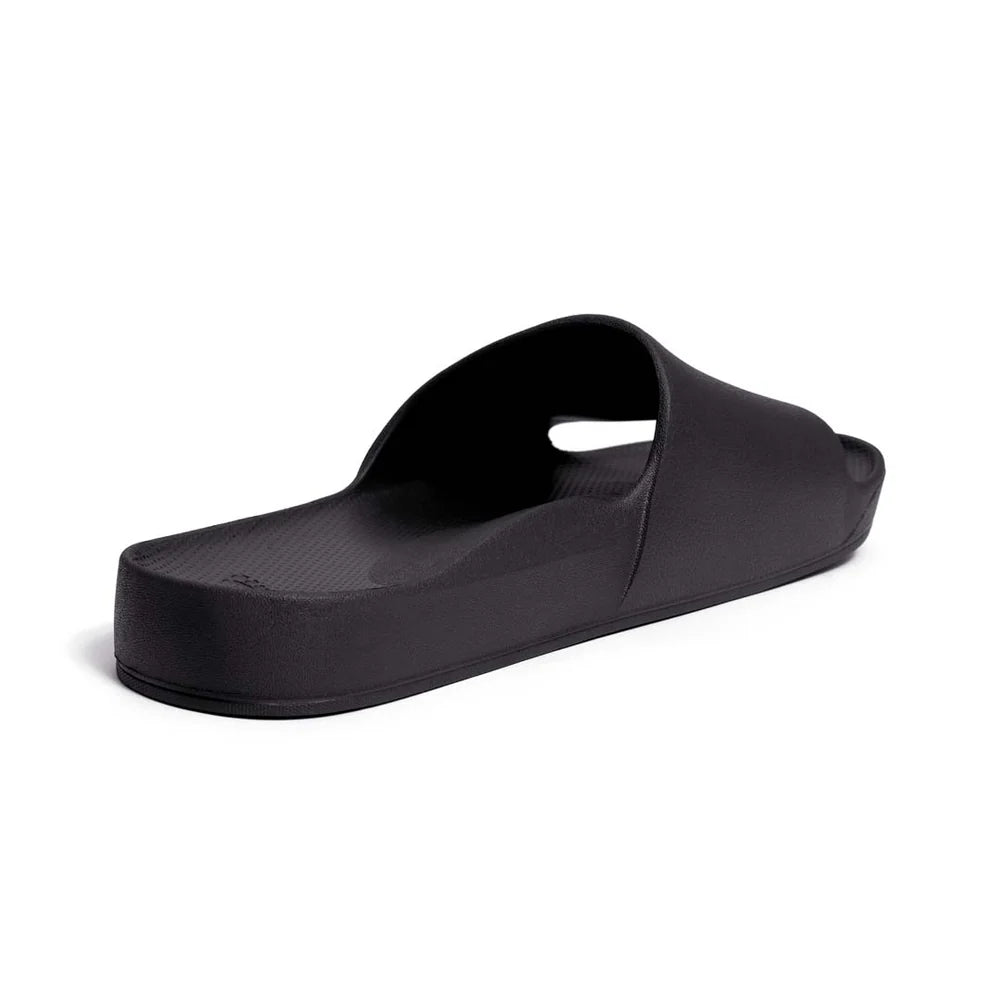 A pair of black arch support slides with a contoured footbed designed for comfort. The slides feature a sleek, minimalist design with a wide strap over the top and a cushioned sole for extra support.