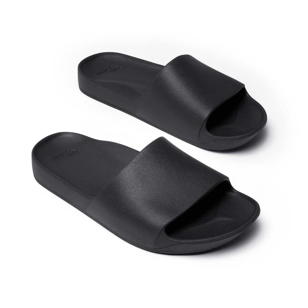 A pair of black arch support slides with a contoured footbed designed for comfort. The slides feature a sleek, minimalist design with a wide strap over the top and a cushioned sole for extra support.