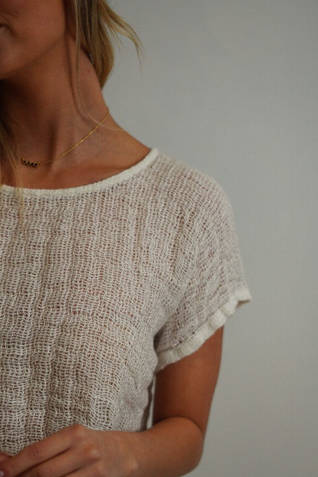 A relaxed, cropped white top made from handloomed stonewashed linen with an open weave fabric, perfect for layering over high-waisted pants or skirts.
