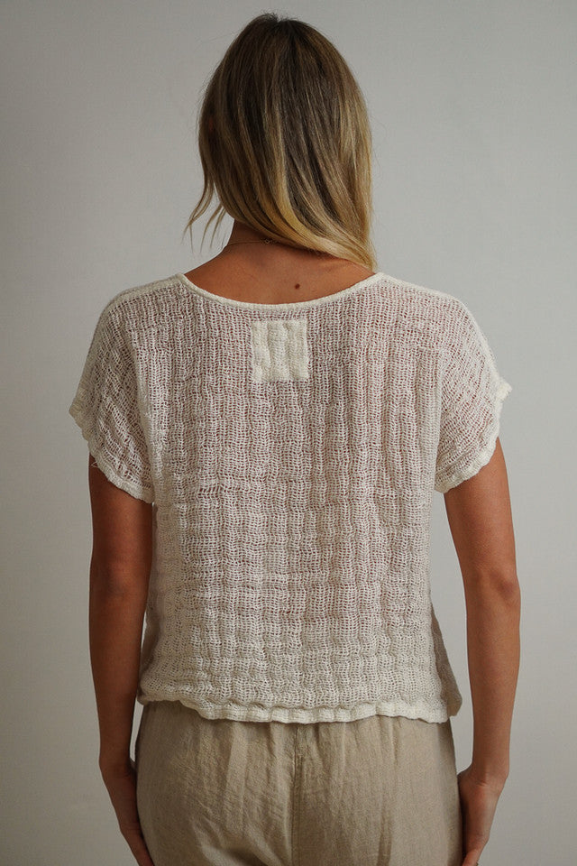 A relaxed, cropped white top made from handloomed stonewashed linen with an open weave fabric, perfect for layering over high-waisted pants or skirts.
