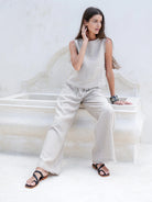 Natural French linen coastal pants with a relaxed fit, elastic waistband, and frayed-edge hem, styled for an effortless summer look.
