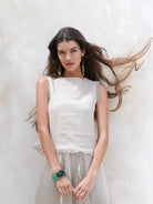 Natural French linen coastal top with a relaxed fit, soft frayed edges, and button opening at the back, styled for easy summer wear.
