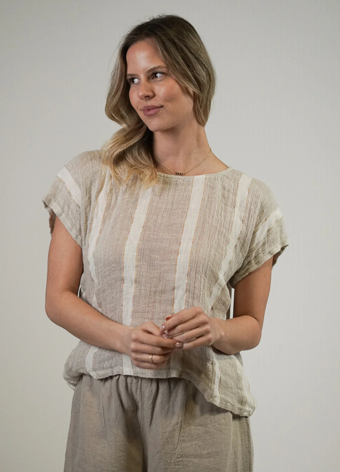 A natural white, box-fit top made from 100% stonewashed mesh linen, featuring short sleeves and a crew neckline. The airy, breathable fabric and relaxed silhouette offer a soft, comfortable feel with subtle gold strand detailing
