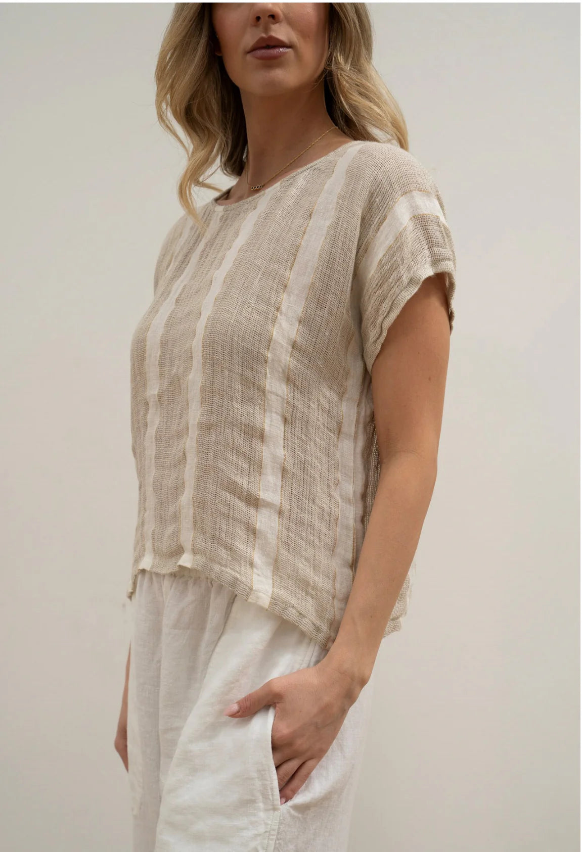 A natural white, box-fit top made from 100% stonewashed mesh linen, featuring short sleeves and a crew neckline. The airy, breathable fabric and relaxed silhouette offer a soft, comfortable feel with subtle gold strand detailing