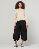 Woman wearing Boom Shankar Cord Guru Pants in soft cotton corduroy with a relaxed balloon-leg fit and 3/4 length style, standing in a coastal boutique setting.
