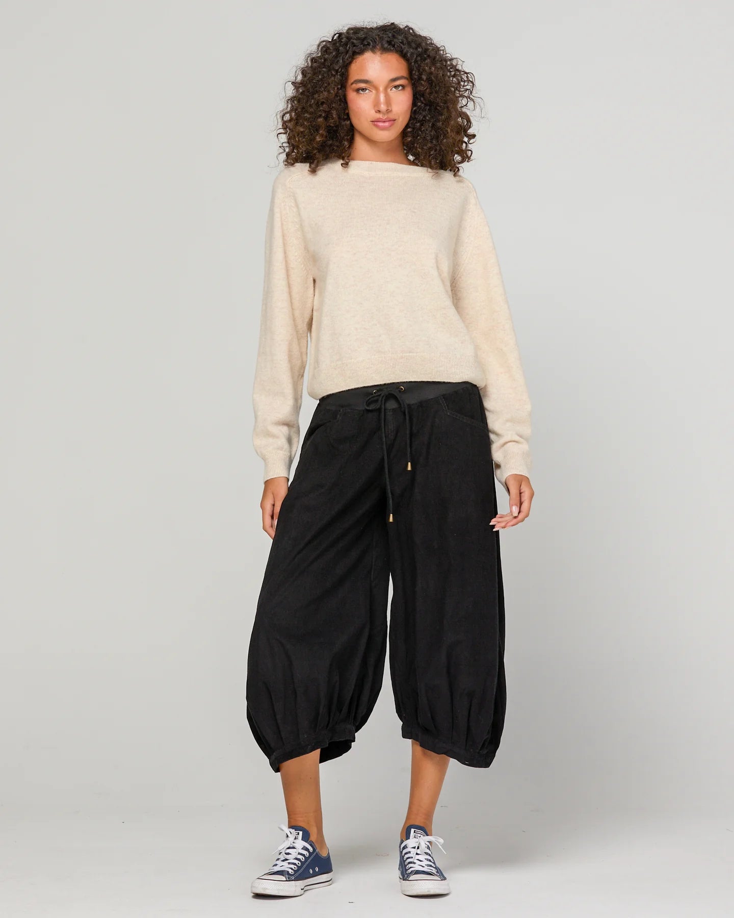Woman wearing Boom Shankar Cord Guru Pants in soft cotton corduroy with a relaxed balloon-leg fit and 3/4 length style, standing in a coastal boutique setting.