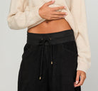 Woman wearing Boom Shankar Cord Guru Pants in soft cotton corduroy with a relaxed balloon-leg fit and 3/4 length style, standing in a coastal boutique setting.