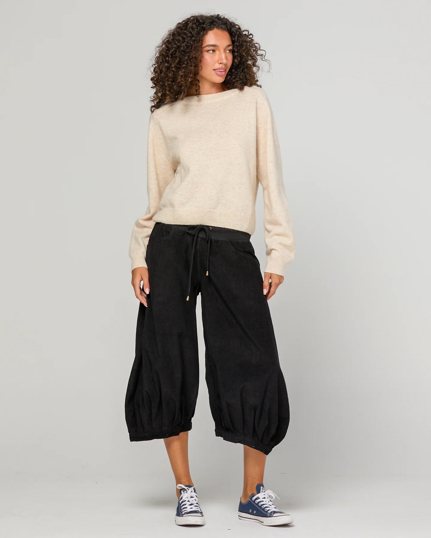 Woman wearing Boom Shankar Cord Guru Pants in soft cotton corduroy with a relaxed balloon-leg fit and 3/4 length style, standing in a coastal boutique setting.