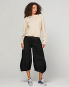 Woman wearing Boom Shankar Cord Guru Pants in soft cotton corduroy with a relaxed balloon-leg fit and 3/4 length style, standing in a coastal boutique setting.