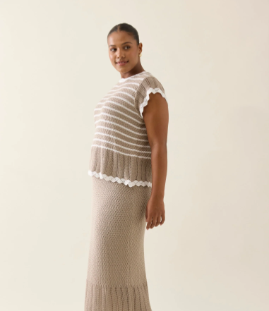 A lightweight, 100% cotton knit top in a soft canvas color, featuring a delicate pointelle texture with subtle horizontal stripes. The top has a relaxed silhouette with scalloped edges along the neckline, sleeves, and hem. A keyhole opening with a tie closure accents the back, adding a refined, feminine detail