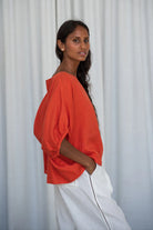 The Lily Pilly Tina Top in vibrant orange spritz is designed with a relaxed silhouette, lightweight feel, and natural linen textured weave.