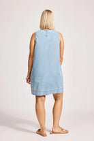 A denim chambray tank dress made from lightweight 100% cotton, featuring exposed shoulders and a slight A-line silhouette. The dress includes contrast topstitching, a button closure at the back neck, a wide cuffed hem, and functional pockets for added practicality. Its breezy, denim-inspired look offers an effortless, summery style