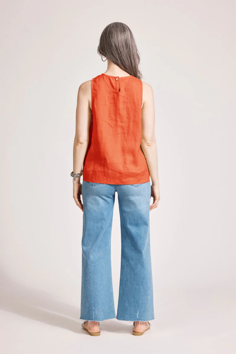 A relaxed, coral-coloured 100% linen tank top featuring exposed shoulders, contrast decorative topstitching, and a soft A-line silhouette. The design includes a wide cuffed hem and a button closure at the back neck, giving the lightweight, breathable top an effortlessly refined look