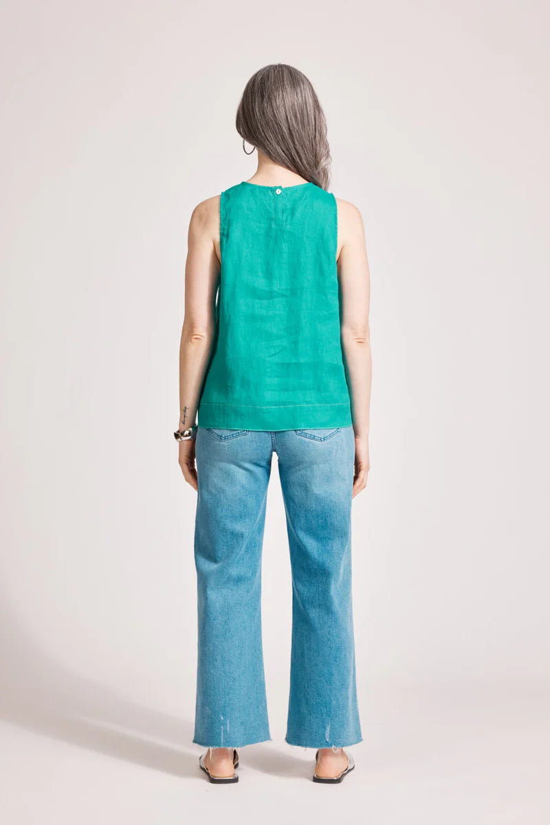 A relaxed, lagoon-coloured 100% linen tank top featuring exposed shoulders, contrast decorative topstitching, and a soft A-line silhouette. The design includes a wide cuffed hem and a button closure at the back neck, giving the lightweight, breathable top an effortlessly refined look