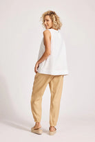 A relaxed, white 100% linen tank top featuring exposed shoulders, contrast decorative topstitching, and a soft A-line silhouette. The design includes a wide cuffed hem and a button closure at the back neck, giving the lightweight, breathable top an effortlessly refined look