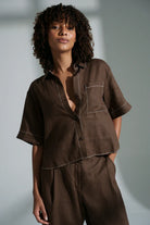 Nika linen shirt in chocolate with relaxed short sleeves, contrast stitching, front pocket, high-low curved hem and corozo buttons.
