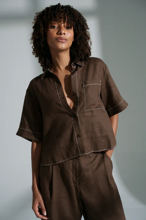 Nika linen shirt in chocolate with relaxed short sleeves, contrast stitching, front pocket, high-low curved hem and corozo buttons.
