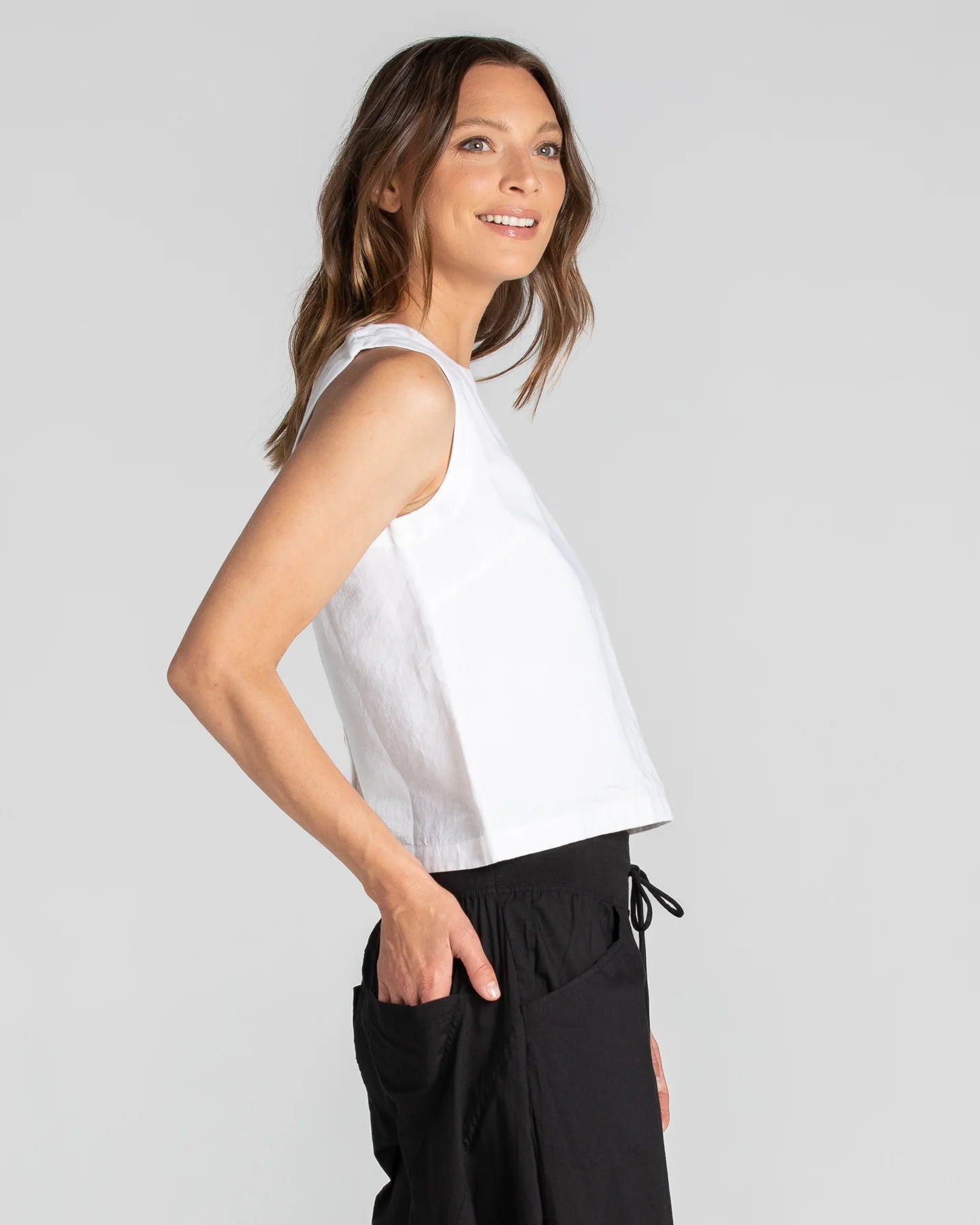 White Rosa Linen Top with a boat neckline, sleeveless design, scooped back hem, and shell button details.