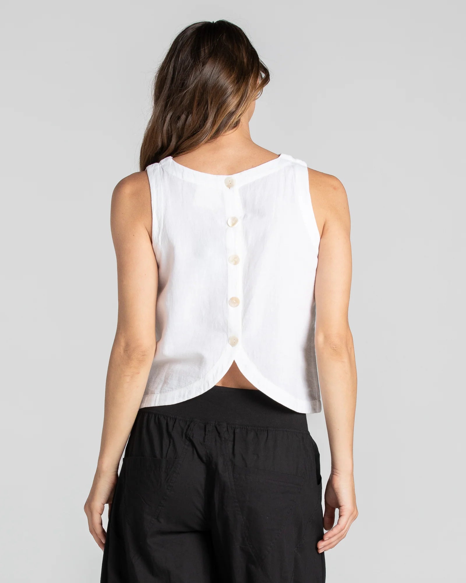 White Rosa Linen Top with a boat neckline, sleeveless design, scooped back hem, and shell button details.