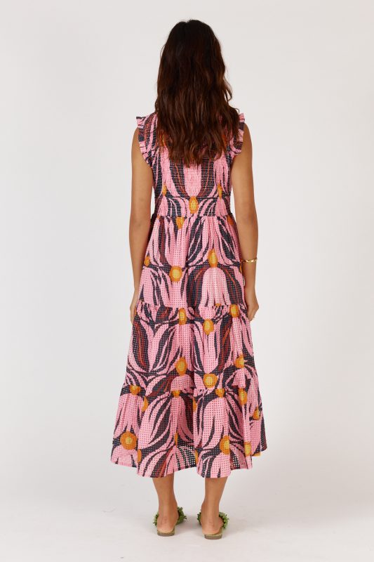 A feminine midi dress in a soft textured Tulip print, made from a cotton-nylon blend. The design features a round neckline with a delicate frill, sleeveless armholes with matching frill trim, and a shirred bodice that contours the figure. A flowing A-line skirt falls to mid-calf, complemented by functional pockets for added ease. The dress offers a relaxed, elegant fit suitable for a variety of occasions