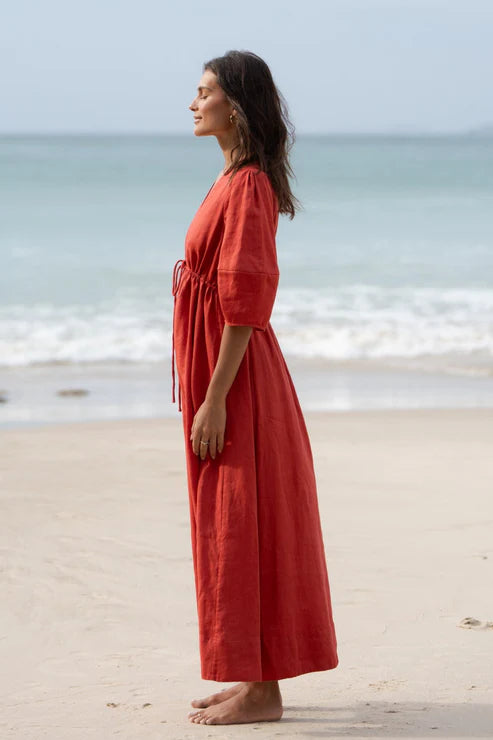 Vida Linen Dress in Hibiscus – A flowy midi-to-maxi linen dress in a vibrant hibiscus hue. Features an adjustable front-tie waistline, oversized bell sleeves, side pockets, and premium French seams for a refined finish.